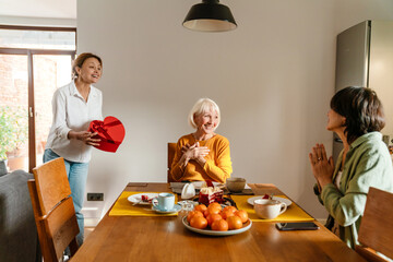 Mature women giving gift box to their friend during birthday lunch
