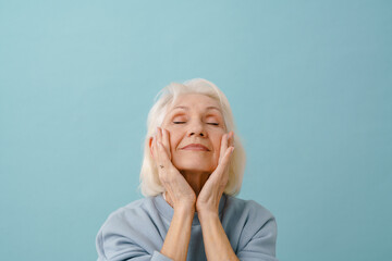 Beautiful smiling senior woman in blue pullover with closed eyes