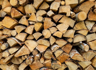 Dry birch firewood stacked in a neat woodpile. A supply of wood for kindling the fireplace. Wooden texture.