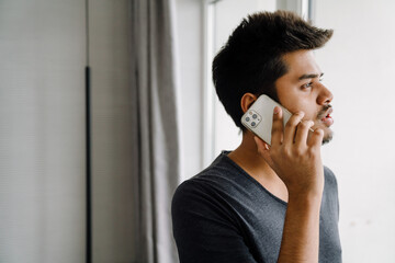 Young handsome indian man talking on phone in sunny room