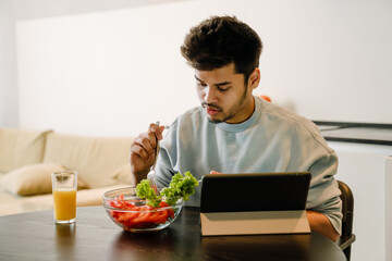 Young indian man with tablet eating fresh salad