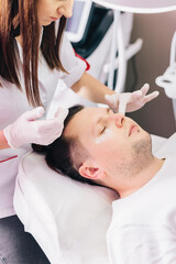 Obraz na płótnie Canvas Cosmetologist applying anesthetic cream on man face in beauty salon