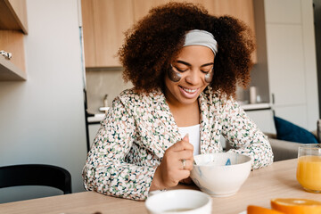 Young beautiful smiling african woman with eye pathces eating breakfast