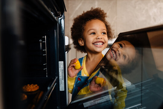 Little African Smiling Boy Standing Next To Oven With Cookies