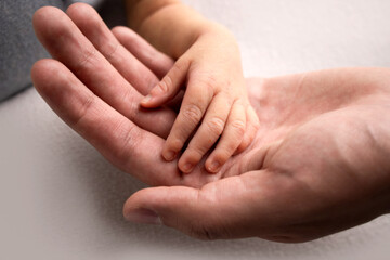 A parent holds the hand of a newborn child. The small hand of the son with tiny fingers lies on the palm of the father. The concept of a happy family. Family hereditary ties.