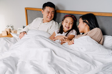 Happy asian family with little girl lying in bed together at home