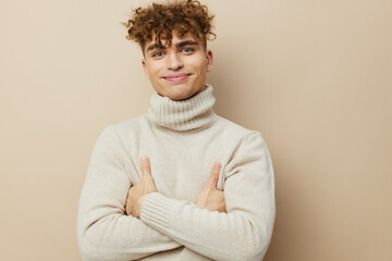 a handsome attractive man stands on a beige background in a light turtleneck and keeps his arms crossed on his chest