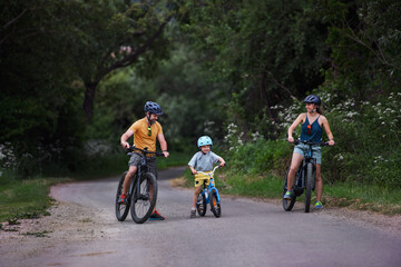 Young family with little child riding bicycles on road in village in summer.