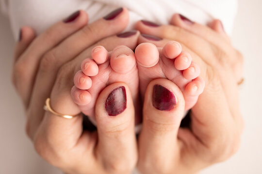 The palms of the parents. A father and mother hold the feet of a newborn child in a white blanket on a white background.. The feet of a newborn in the hands of parents. Photo of foot, heels and toes