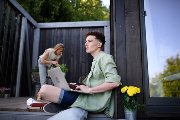 Happy young couple with laptop resting outdoors in a tiny house, weekend away and remote office concept.
