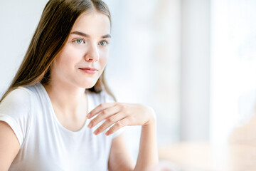 Fototapeta premium Teenage girl with hand near face sitting sitting indoor.
