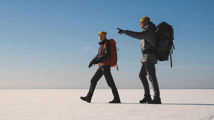 The couple of tourists with backpacks traveling through the snow field