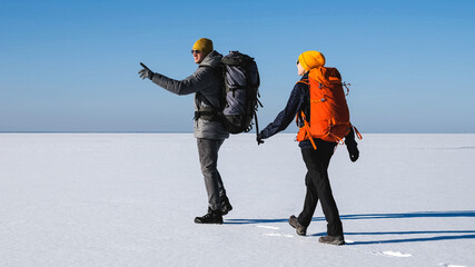 The man and woman with backpacks traveling through the snow field