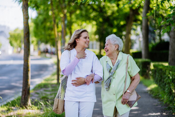 Portrait of caregiver with senior woman on walk in park with shopping bag, looking at caemra.