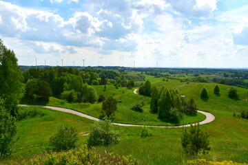 A view of an asphalt road leading uphill towards the top of a hill or mountain, with trees, herbs,...
