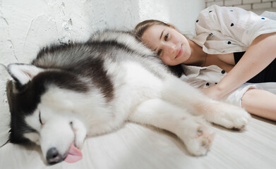 Fototapeta na wymiar Sleeping alaskan malamute big dog and young woman lying on floor. Beautiful girl love pet. Portrait of female owner and adorable malamute happy close friend, together have fun at home in bedchamber.