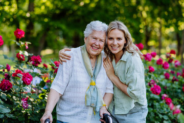 Portrait of adult granddaughter with senior grandmother on walk in park, with roses at background