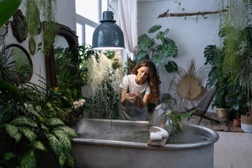 Focused woman gardener taking care about aquatic plant in greenhouse, holding houseplant under...