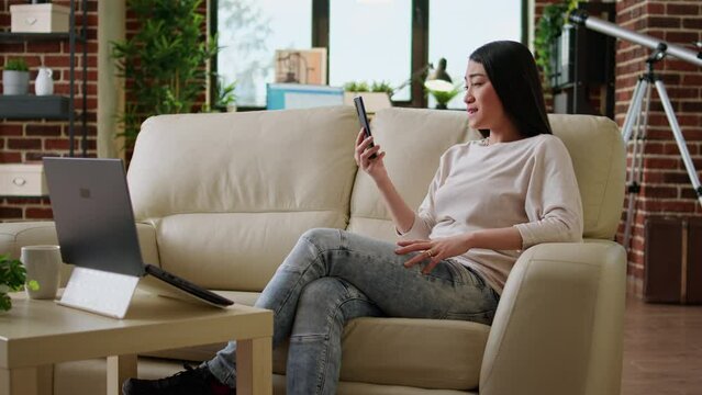 Smiling heartily woman discussing with work colleague on phone video call while working remotely. Happy asian freelancer on smartphone video call talking with client about job description.