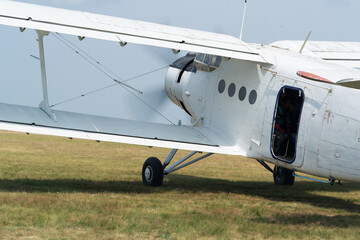 An An-2 plane starts its engine before the flight on a grass airfield. Back view.