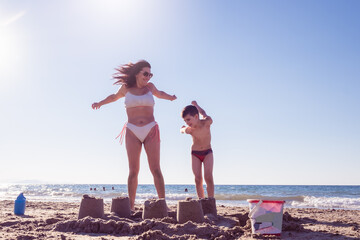 mom and son play at the beach making a sand castle together and they jump happily