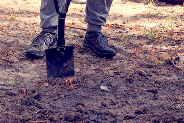 Black shovel in human hands. Man digs soil with a shovel in the forest.