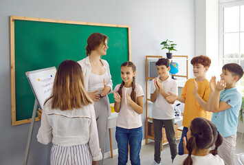 Learning while playing. Children in primary school in creative lesson learn by playing games together with teacher. Friendly female teacher and schoolchildren in classroom clapping their hands. - obrazy, fototapety, plakaty