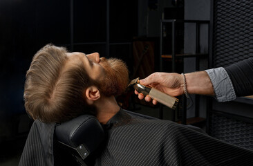 Young man with trendy haircut and beard at barber shop. Barber does the hairstyle and beard trim.
