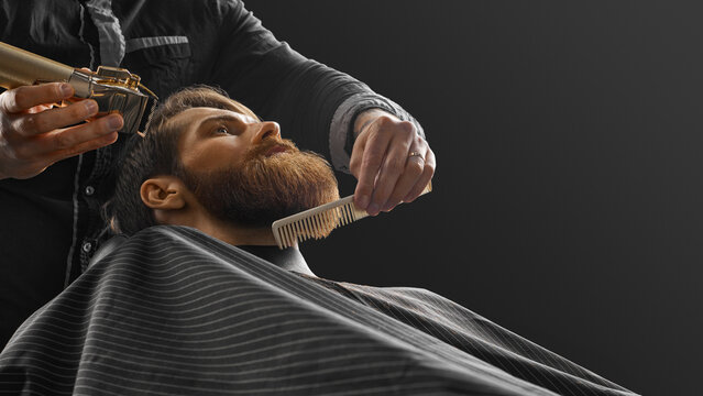 Professional hairdresser shaving client in barbershop. Trendy and stylish beard styling and cut.