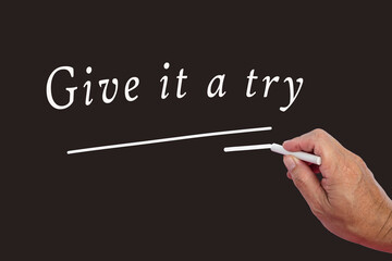 Male hand writes in white chalk pencil the word Give It A Try.