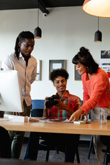 Biracial photographer discussing with multiracial colleagues in meeting at creative office