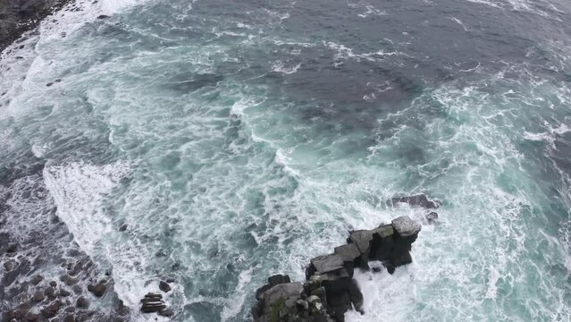Aerial view of blue irish ocean, high and deep slope. Travel destination Ireland cliffs, dark rocks, seagulls flying, rough sea in summer cloudy day. Waves crashes into rocks , Ireland