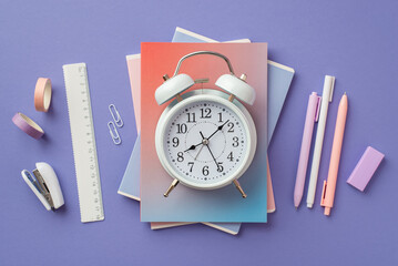 Back to school concept. Top view photo of alarm clock over colorful diaries pens adhesive tape...