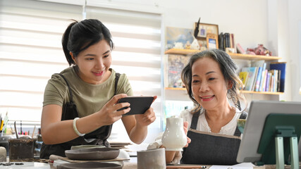Young female pottery shop owner taking photo of product for upload to website online shop. Online...