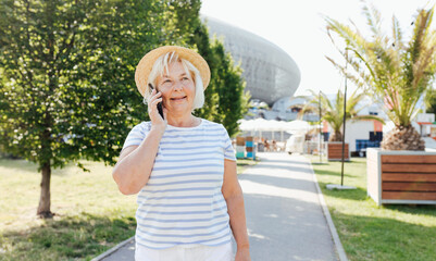 Beautiful Mature woman in trendy wear spending time on street using smartphone. Happy senior talking on the mobile phone, warm sunny day. Urban lifestyle concept, technology banner