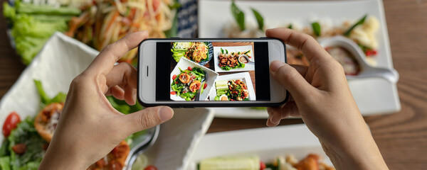 Thai food. The hand is using a mobile phone to take a picture of food on the dining table in the...