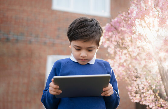 Happy Kid Holding Tablet Pc Standing Outside Waiting For School Bus, Child Boy Playing Game Online Or Reading Story On Internet, Preschool Boy Learning With Modern Technology,Back To School Concept