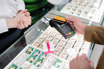 Cropped view of customer paying with credit card near gift and seller in jewelry shop.
