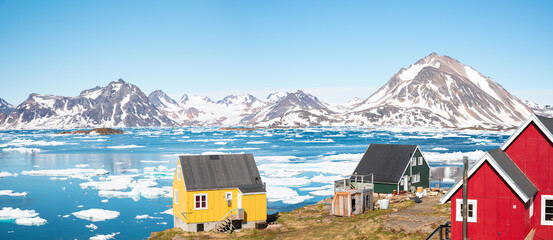 Panoramic view of colorful Kulusuk village in East Greenland - Kulusuk, Greenland - Melting of a iceberg and pouring water into the sea - obrazy, fototapety, plakaty