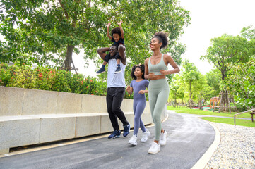 Happy African American family in sportswear running in public park. father carrying son with mother and daughter. Family exercising together concept.