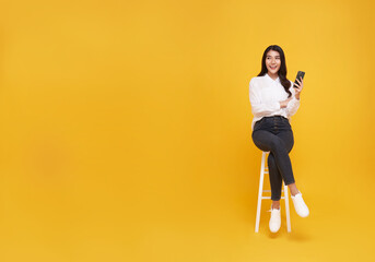 Happy young Asian woman showing mobile phone. While her sitting on white chair and looking on...