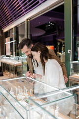 Man looking at showcase while girlfriend pointing with finger in jewelry shop.