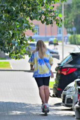 A young woman rides an electric scooter on the sidewalk on a summer day