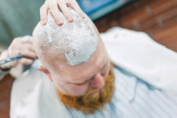 The nape of bearded bald man is being shaved with a razor.