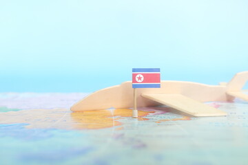 Selective focus of North Korean flag in blurry world map and wooden airplane model. North Korea as travel and tourism destination concept.