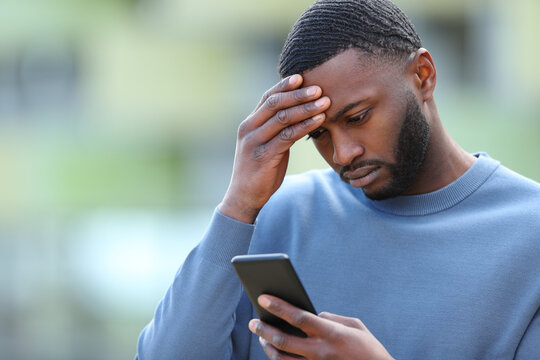 Worried black man checking phone in the street