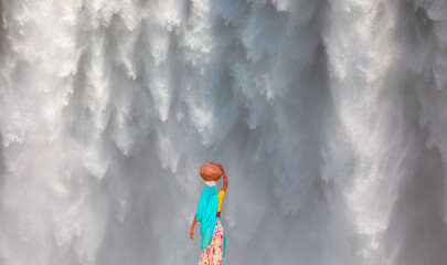 Global warming concept - An indian woman in traditional dress carrying water - close-up of famous Skogafoss waterfall - Iceland