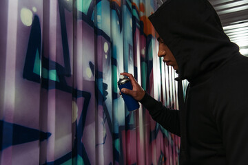 Fototapeta na wymiar Side view of african american vandal in hood drawing graffiti on wall