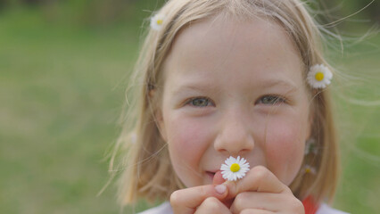 A girl with daisies in her hair and hands is smiling. The concept of youth and beauty and hair and body care