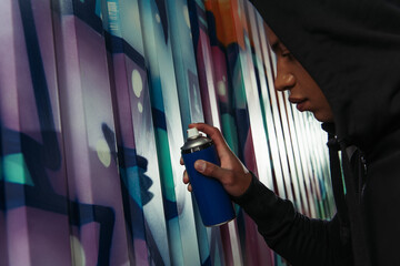 Side view of african american hooligan in hoodie drawing graffiti on wall on urban street - obrazy, fototapety, plakaty